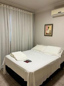 Schlafzimmer mit einem Bett mit weißer Bettwäsche und einem Fenster in der Unterkunft Casa com churrasq, piscina e Wi-Fi em Criciuma SC in Criciúma