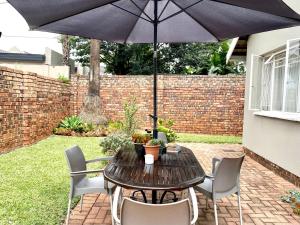 einen Holztisch mit Stühlen und einem Sonnenschirm in der Unterkunft Willows Garden Cottage in Pretoria