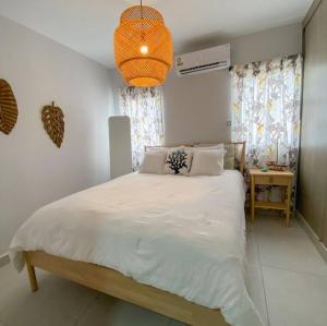 um quarto com uma grande cama branca e um lustre em Relaxing condo near airport PUJ Pool/Wi-fi em Punta Cana