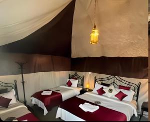 a bedroom with two beds with red and white pillows at Exceptional Luxury Camp in Merzouga