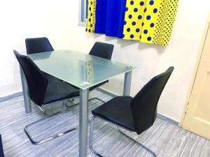 a glass table with four black chairs in a room at Chic Appart Climatisé Wifi 1er Etage in Lomé