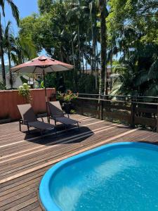 a deck with a pool and two chairs and an umbrella at Casario 1915 Pousada in Morretes