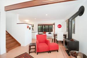a living room with a red chair and a staircase at Byron Bay Accom - Alkira 1/32 Alcorn St in Suffolk Park