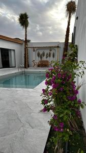 a swimming pool with purple flowers next to a building at شاليه أوڤال Oval Chalet in Al Jubail