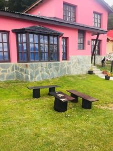 ウシュアイアにあるCasa Las Violetas, Ushuaiaのピンク色の家の前の芝生に置かれた2つのベンチ