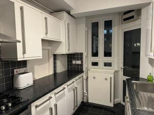 a kitchen with white cabinets and a black counter top at 3 Bedroom Entire Flat, Primrose Hill in London
