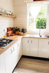 cocina con armarios blancos, fregadero y ventana en The Old Cottage - Country Couples Retreat, en Tomerong