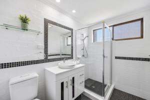 a white bathroom with a sink and a shower at Quaint 2-Bed Beach Abode with Ocean Views in Alexandra Headland