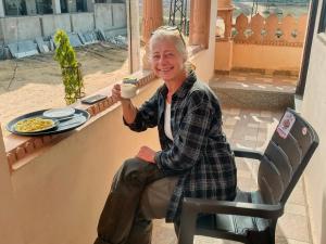 una mujer mayor sentada en una silla sosteniendo una taza de café en The Vantage Haveli, en Sawāi Mādhopur