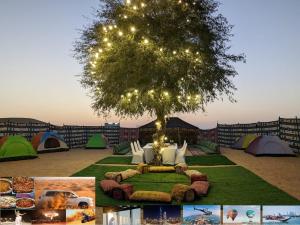 een boom met lichten erop en tenten bij Enjoy The Leisure of Overnight Campsite in Dubai Desert Safari With Complementary Pick up in Dubai