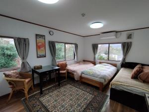 a room with two beds and a desk and windows at Pension Izukogen in Ito