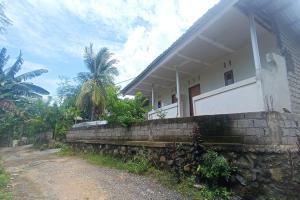 ein weißes Haus mit einer Steinmauer neben einer unbefestigten Straße in der Unterkunft OYO 93729 Radesa Family Homestay in Kuta Lombok