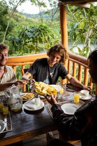 grupa ludzi siedzących przy stole jedzących jedzenie w obiekcie Dave the Cave Eco Lodge and Cultural Campsite w mieście Rubirizi