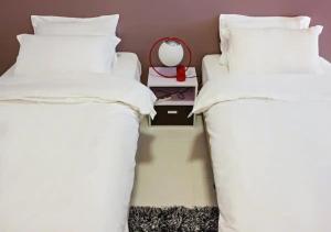 dos camas con sábanas blancas y una mesita de noche entre ellas en Three Storey Garden Home at Bukit Gambir 18ppl, en Gelugor