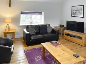 a living room with a black leather couch and a tv at Murton Cottage in East Ord