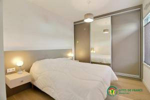 ein Schlafzimmer mit einem weißen Bett und einem großen Spiegel in der Unterkunft RÉF 256 - LARMOR-PLAGE T2 en RDC plein bourg avec terrasse sur rue principale et parking in Larmor-Plage