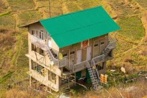 a house with a green roof on a hill at Dhauladhar Woodhouse in Malotha