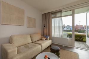 a living room with a couch and a large window at Welcome in - Appartementen Kurhaus - Nieuwstraat 1 Zoutelande, nabij strand, terras, sauna in Zoutelande