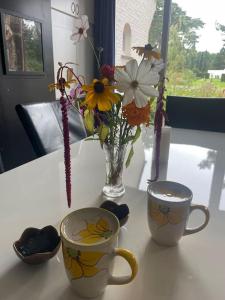 duas chávenas e um vaso de flores numa mesa em Vier sterren woning met bubbelbad bij bos en meer em Maasmechelen