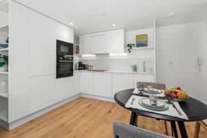 cocina con armarios blancos, mesa y sillas en Chic Urban Retreat: Modern Apartment in Eastbourne, en Eastbourne