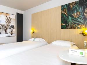 トロワにあるibis Styles Troyes Centreのベッド2台、テーブル、絵画が備わるお部屋