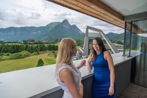 two women standing on a balcony with mountains in the background at Narzissen Vital Resort Bad Aussee in Bad Aussee
