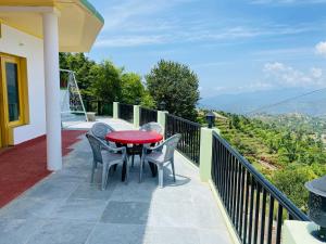 Un patio con una mesa roja y sillas en un balcón. en Sunstone House, en Mukteshwar