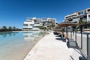 - une piscine avec des chaises et un parasol et certains bâtiments dans l'établissement Ocean Homes by Ĥ - Playa de los Haraganes HOHH7104P70, à Isla Canela