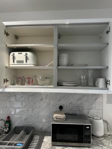 a kitchen with a microwave and some dishes on shelves at Town Centre Studio Flat in Merthyr Tydfil +5 photos