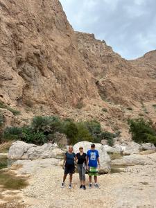 three people standing on rocks in front of a mountain at Atlas Wadi Shab in Sur