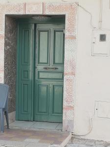 une porte verte sur un bâtiment avec une chaise à l'avant dans l'établissement Darna, à El Haouaria