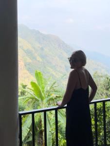 kobieta stojąca na balkonie z widokiem na góry w obiekcie Nature Green Hotels On Rock Home Ella w mieście Ella