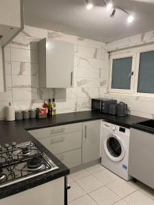 Well-preserved cozy1BR flat in LCY with free parking في لندن: مطبخ مع موقد وغسالة ملابس