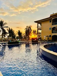 a pool at a resort with a sunset in the background at Apartamento de lujo frente a playa Jacó-3 BD/ 2 BA in Jacó