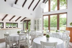 una sala da pranzo con tavoli e sedie bianchi e finestre di Cottage 2 im Natur-Resort Pool, Schwimmteich & Sauna a Kiskunmajsa