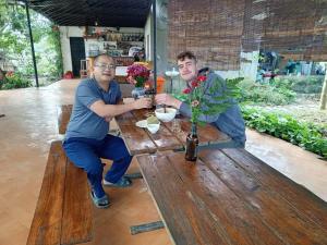 dos hombres sentados en una mesa de madera con flores en Đảo Chè Thanh Chương - Homestay Gió Lào, en Trai Ðỏ
