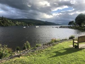 a bench sitting on the grass next to a lake at Annie’s Flat in Aberfeldy