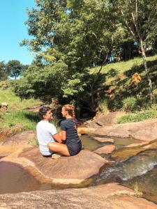 mężczyzna i kobieta siedzący na kamieniu przy strumieniu w obiekcie Aconchego na montanha com BANHEIRA de imersão e 5 suítes 7,5km do centro Águas de Lindóia w mieście Águas de Lindóia