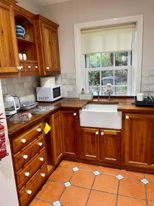 eine Küche mit Holzschränken, einem Waschbecken und einem Fenster in der Unterkunft Station Road Cottage in Burgh by Sands