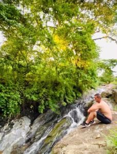 um homem sentado numa rocha ao lado de uma cascata em Aconchego na montanha com BANHEIRA de imersão e 5 suítes 7,5km do centro Águas de Lindóia em Águas de Lindoia