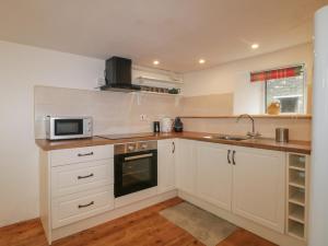 a kitchen with white cabinets and a sink and a microwave at Dunridge Cottage in Yelverton