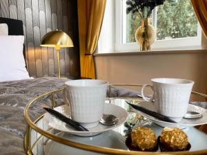 2 tasses et soucoupes sur une table en verre à côté d'un lit dans l'établissement NEU! Art Deco Design-Luxus-Apartment, am Markt, Garten, à Gera