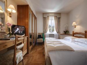 Habitación de hotel con 2 camas, escritorio y TV. en Hotel De La Poste, en Cortina dʼAmpezzo