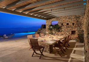a dining table with chairs and a stone wall at Lethos Villa - Tinos in Kionia