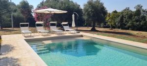 a swimming pool with four chairs and an umbrella at Villa Morea-Relax in piscina in Putignano