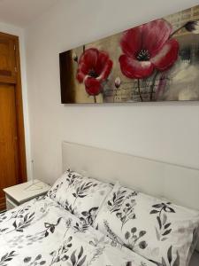 1 dormitorio con 1 cama y una pintura de flores rojas en APARTAMENTOS SURYCAN, en San Bartolomé