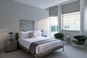 a white bedroom with a bed and two green chairs at AKA Marylebone in London