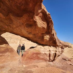 two people standing under a rock formation in the desert at Desert Dream Camp in Wadi Rum