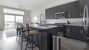 Landing Modern Apartment with Amazing Amenities (ID1802X92) في هيوستن: مطبخ مع دواليب خشبية وجزيرة مطبخ مع كراسي بار
