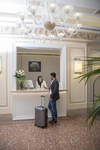 a man with a suitcase and a woman at a counter at Hotel Grande Italia in Chioggia